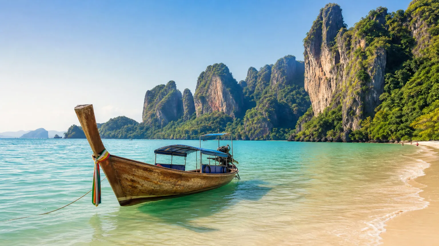 Longtailbåd ved turkis vand og kalkstensklipper på en strand i Krabi, Thailand