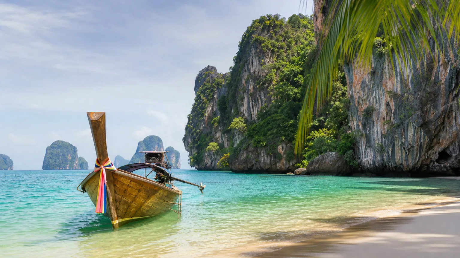 Longtailbåd ved turkis vand og kalkstensklipper på en tropisk strand i det sydlige Thailand
