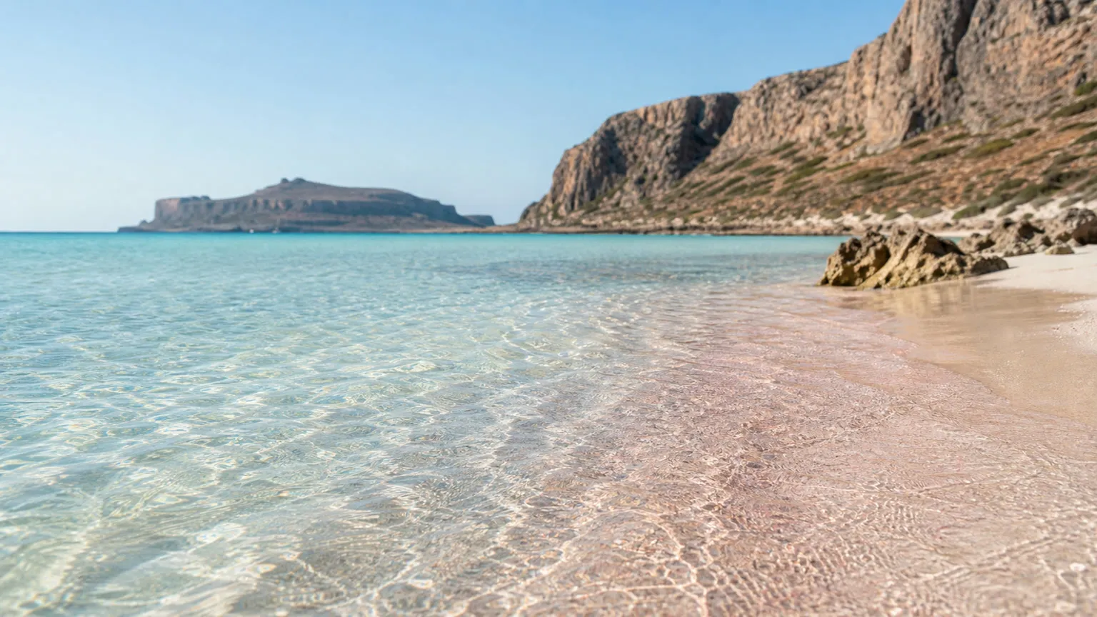 Balos Lagune på Kreta med klart turkisblåt vand, lyserødt sand og klipper i morgensol