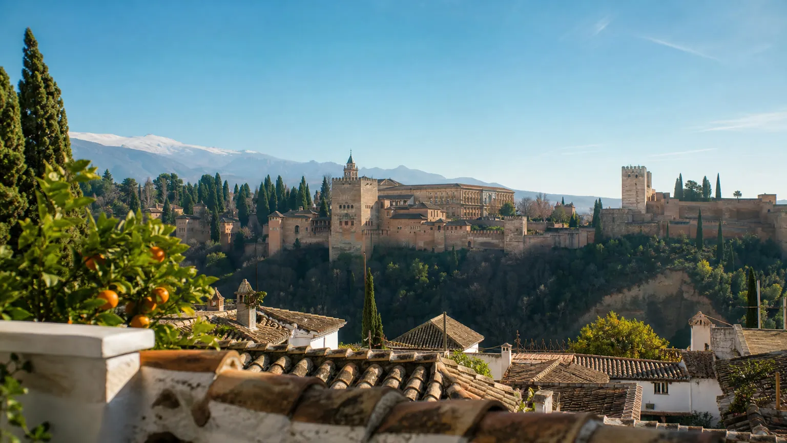 Alhambra i Granada set fra Albaicín med appelsintræer, tegltage og Sierra Nevada i baggrunden